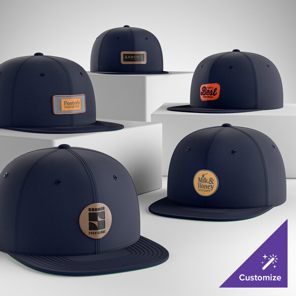 A collection of customizable navy blue 6-panel flat bill snapback caps with various logo patches on the front.