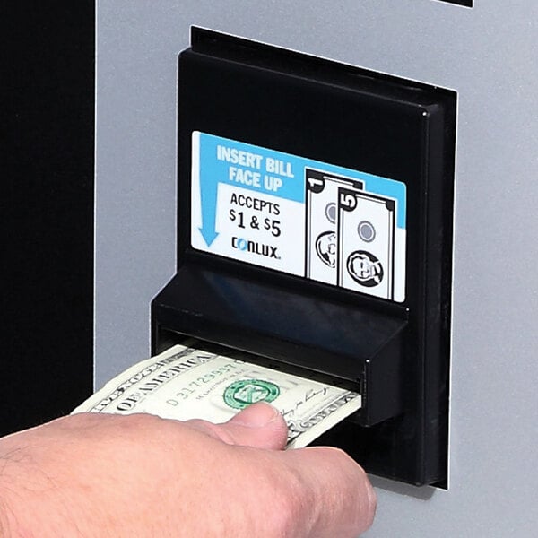 A hand inserting money into a laundry vending machine.