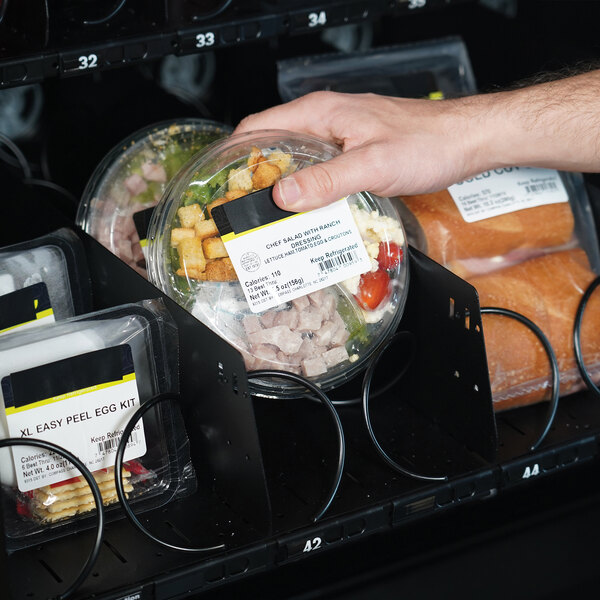 A hand putting a plastic container of food in a frozen/cold vending machine.