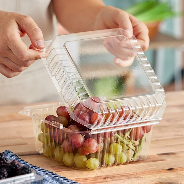 A person holding a clear plastic D&W Fine Pack clamshell container of grapes.