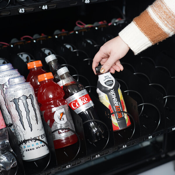 A person using a white hand to put a bottle of soda into a vending machine.