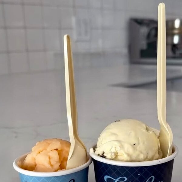 A pair of blue paper cups filled with frozen desserts, each with a beige-colored up-cycled natural spoon inserted.