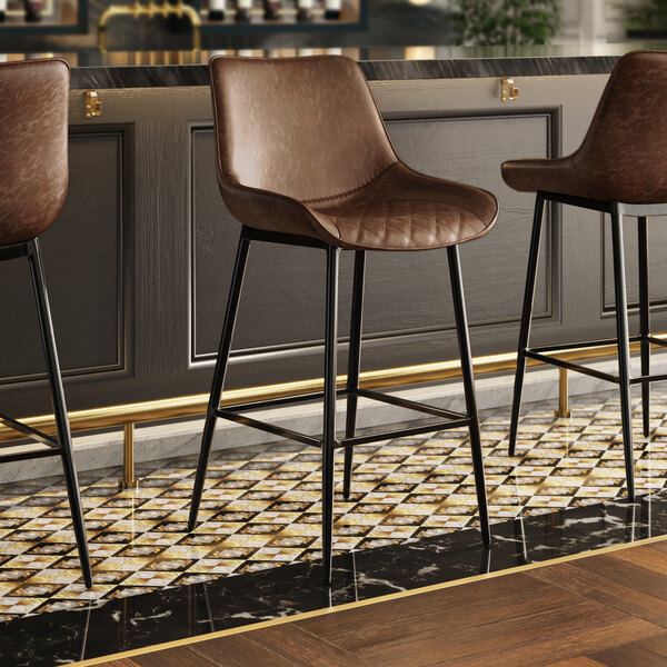 Three Lancaster Table & Seating brown leather bar stools with black metal legs and tufted seats.