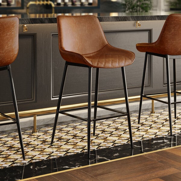 A row of Lancaster Table & Seating black barstools with cognac tufted vinyl seats.