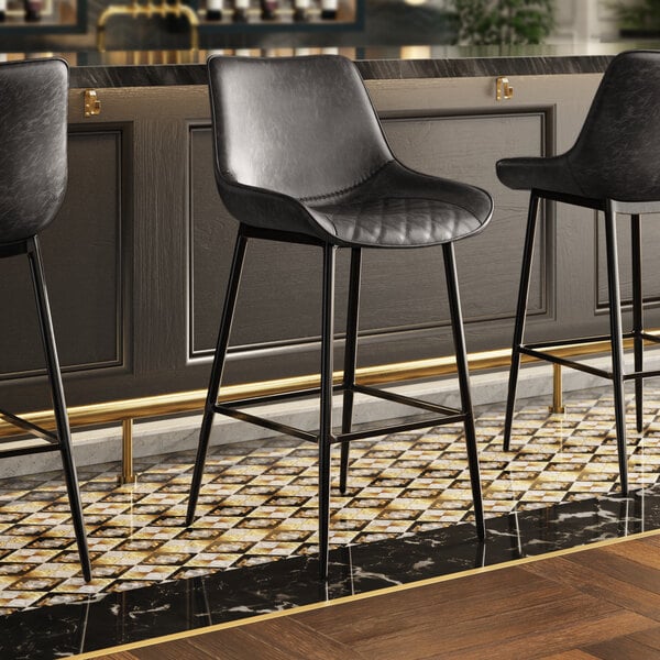 Three Lancaster Table & Seating black bar stools with black tufted vinyl seats at a bar.