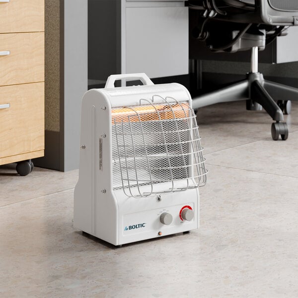 A portable white electric radiant and forced air heater with a protective metal grill and control knobs, placed on an office floor.