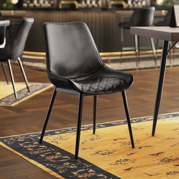 A Lancaster Table & Seating black chair with black tufted vinyl seat sits in front of a table in a restaurant.