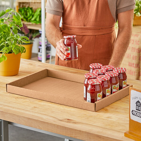 A man holding a jar of strawberry jam on a Kraft corrugated tray.