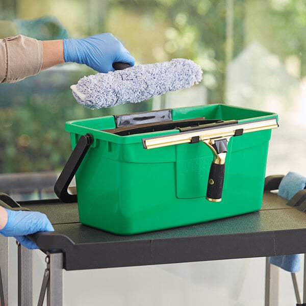 A person wearing blue gloves using a green Unger Pro window cleaning bucket.
