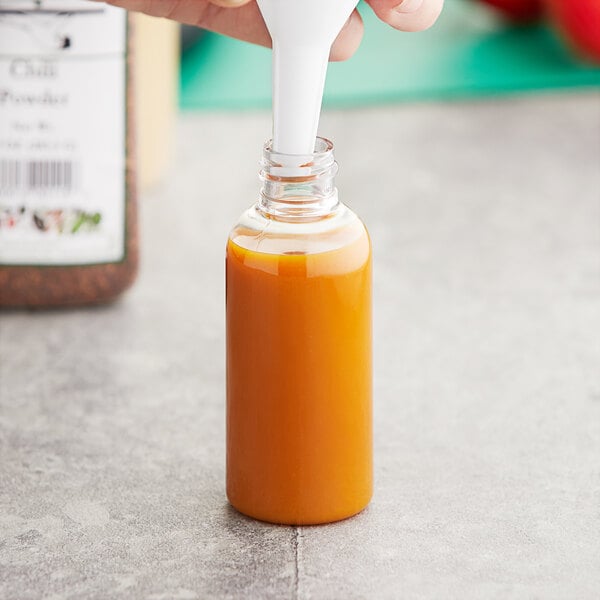 A person's hand pouring orange liquid from a white spoon into a 2 oz. PET Boston round bottle.