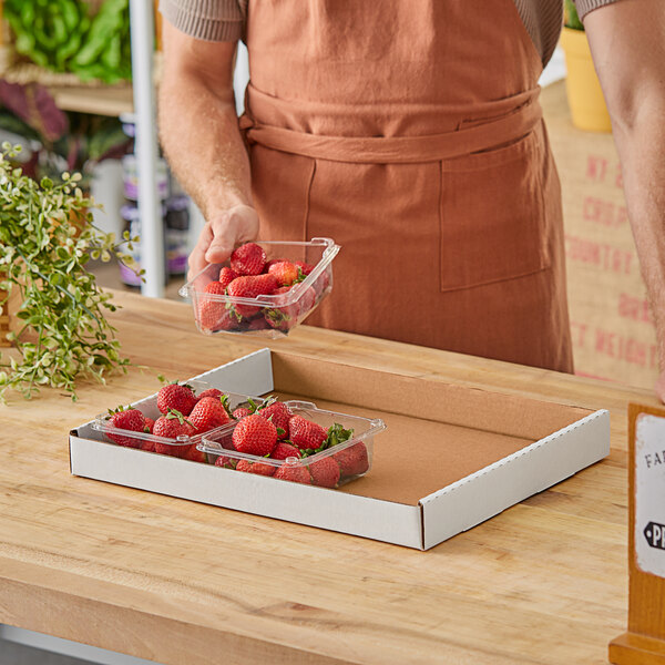 A man holding a white corrugated half tray of strawberries on a table.