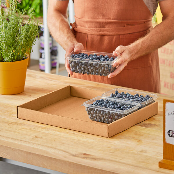 A man holding a Choice Kraft Corrugated Half Tray filled with blueberries.