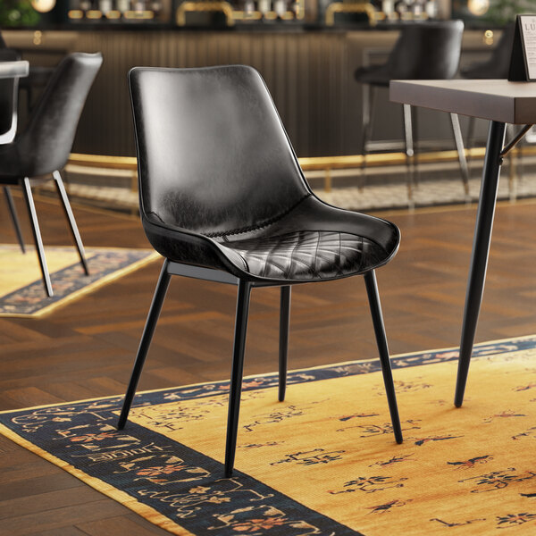 A Lancaster Table & Seating black chair with black tufted vinyl seat sits in front of a table in a restaurant dining area.