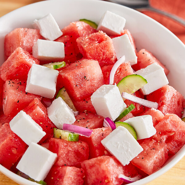 A bowl of watermelon salad with a close up of watermelon and cheese.