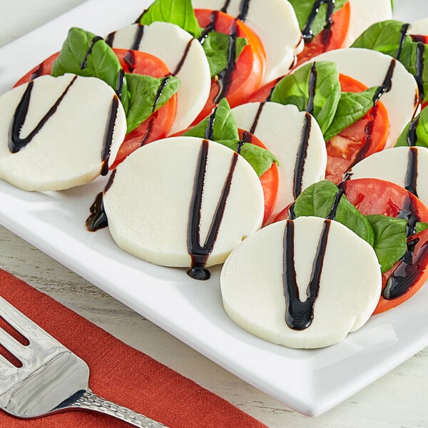 A plate of sliced tomatoes with basil and black pepper topped with Plant Ahead Vegan Mozzarella.