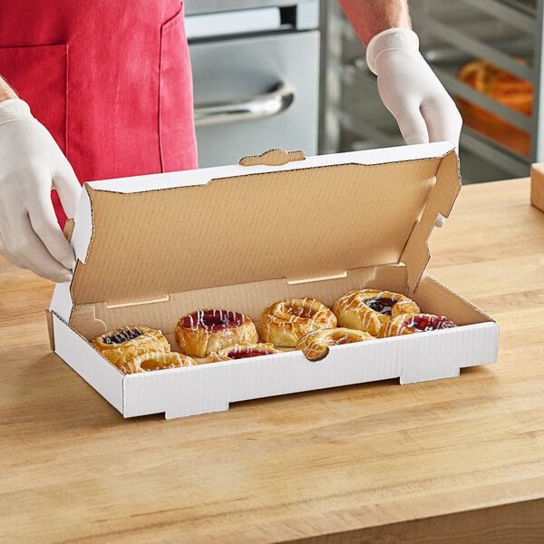 A person in a white apron holding a Choice white corrugated bakery box filled with pastries.