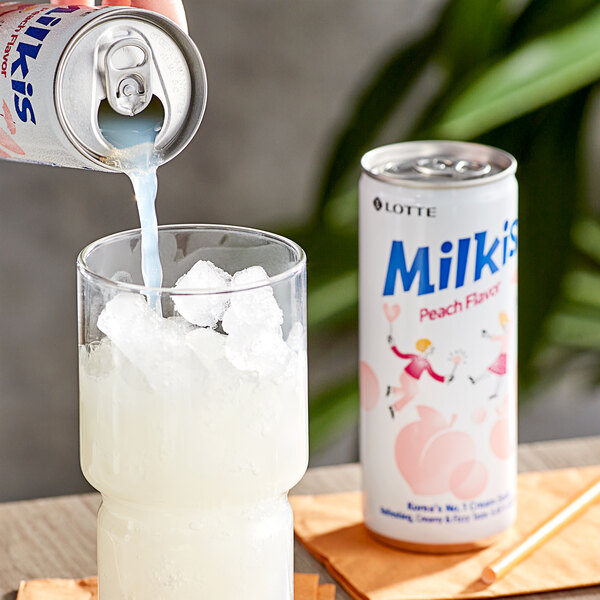 A hand pouring Milkis Peach Milk Soda from a can into a glass of ice.