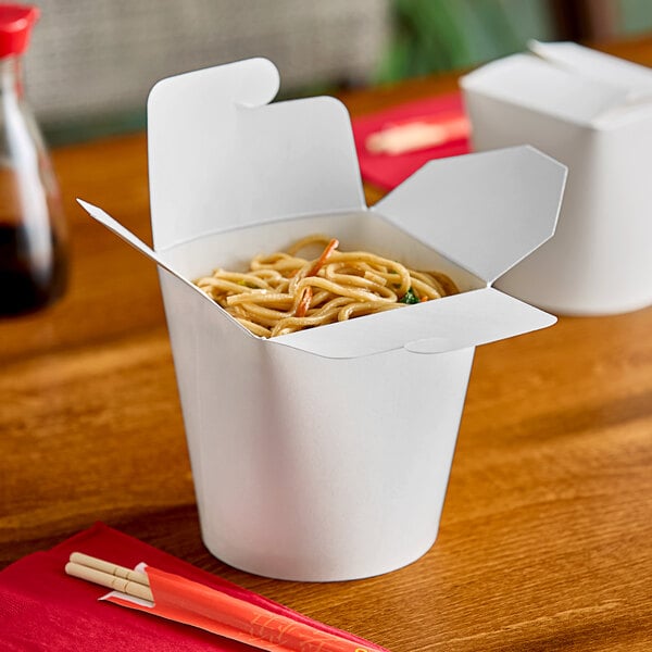 A close-up of Emperor's Select white microwavable take-out container filled with noodles on a table.