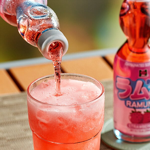 A bottle of Hana Ramune Strawberry Soda pouring a red drink into a glass.