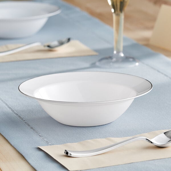 A white bowl with a silver band on a table with a spoon.