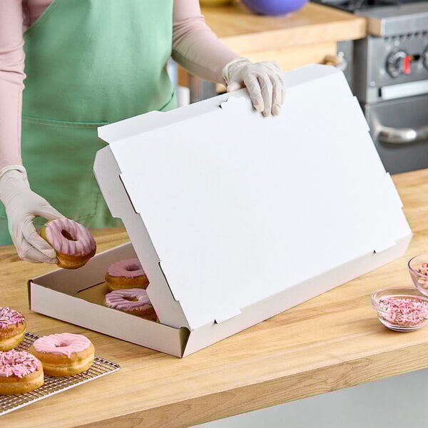 A woman in a green apron putting pink donuts into a white bakery box.