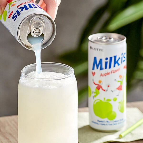 A hand pouring Milkis Apple Milk Soda into a glass with a straw.