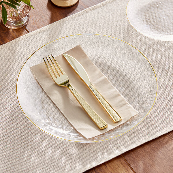 A Visions clear plastic coupe plate with a gold fork and knife on it.