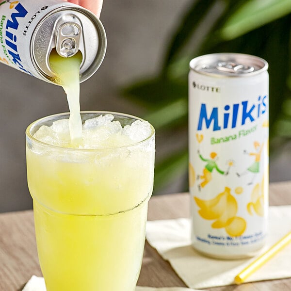 A hand pours Milkis Banana Milk Soda into a glass.