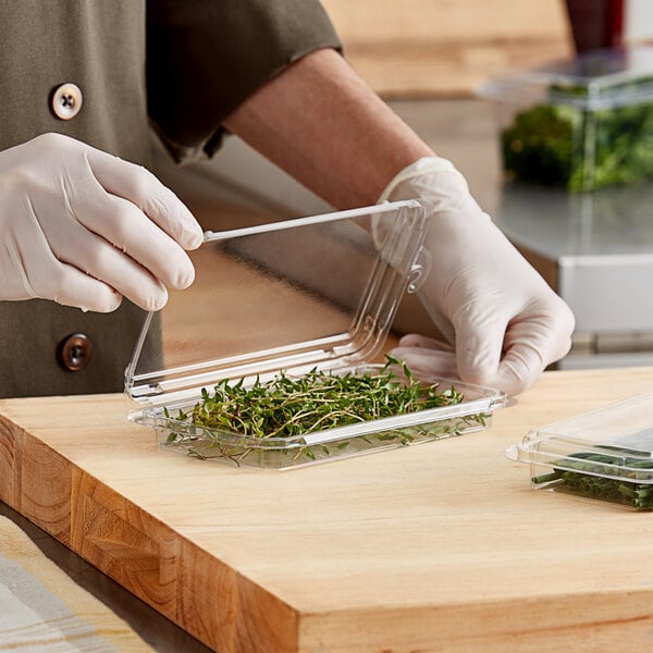 A person in gloves cutting herbs into a clear plastic container.