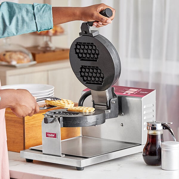 A person making waffles in a commercial Estella waffle maker.