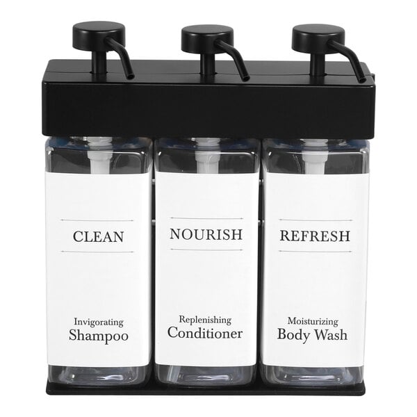 A white wall-mounted Dispenser Amenities holder with three black rectangular bottles inside.