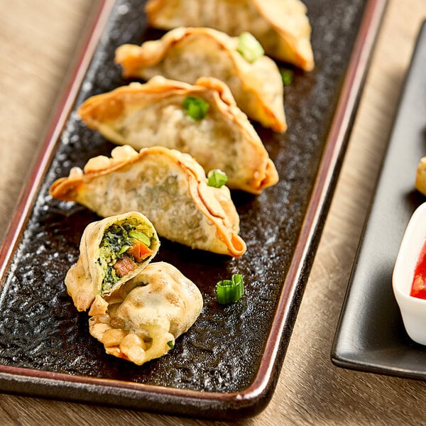 A plate of Chef One kale, mixed vegetable, and tofu dumplings with dipping sauce.