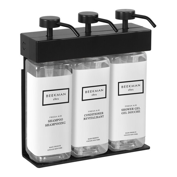 A black wall-mounted dispenser with three rectangular bottles with black and white labels.