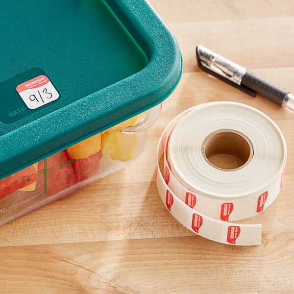 A plastic container with food in it next to a roll of DayMark Dissolvable Wednesday labels.