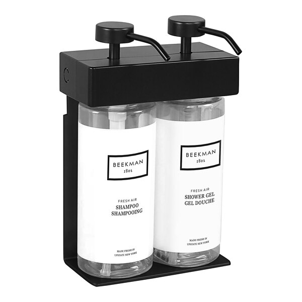 A black Dispenser Amenities wall mounted shower dispenser with two white oval bottles with black text.