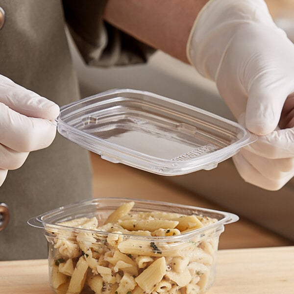 A gloved hand holding a clear plastic Good Natured deli container of pasta.