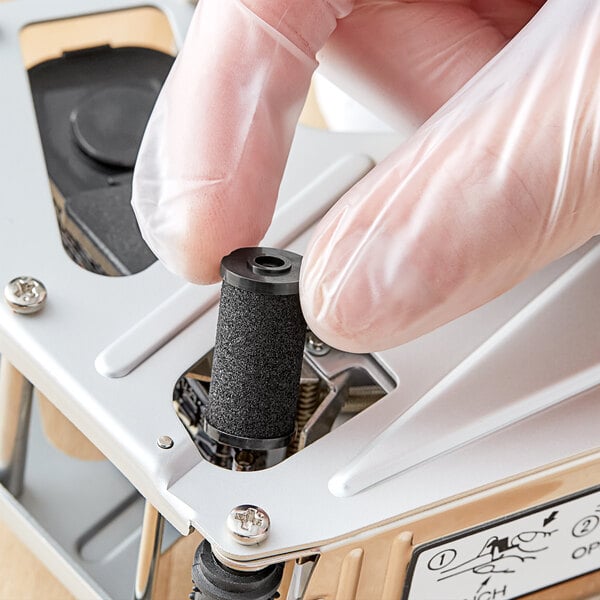 A person wearing gloves removes the black ink roller from a small DayMark Speedy Mark 3 device.