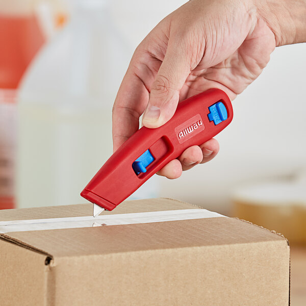 A hand using a red Allway Tools plastic vanishing knife to open a box.