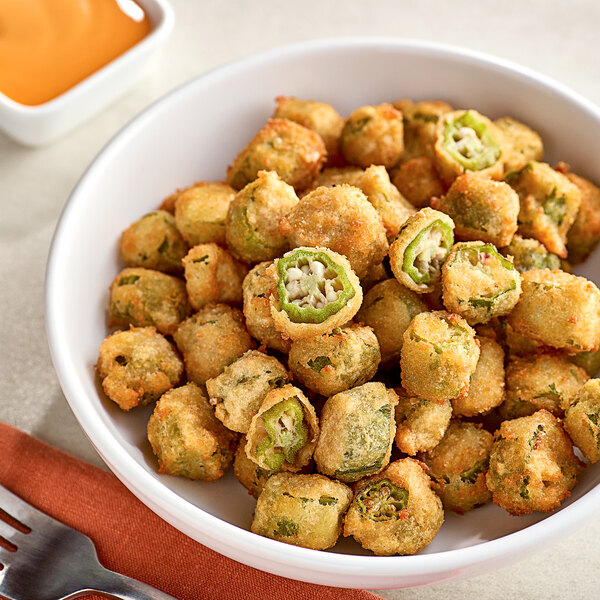 A bowl of Stilwell heavily breaded fried okra pieces with dipping sauce.