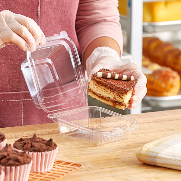 A woman in gloves holding a clear plastic container with a piece of cake inside.