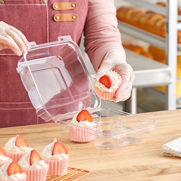 A woman in a pink apron holding a Good Natured clear plastic container with a cupcake with a strawberry on top.