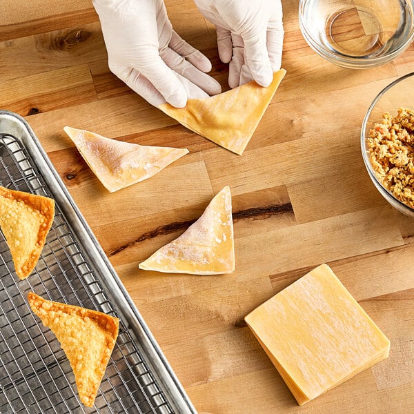 A gloved hand holds a triangle-shaped wonton wrapper.