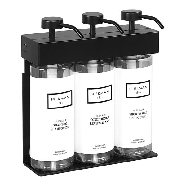 A black wall-mounted dispenser with three oval bottles with black and white labels.