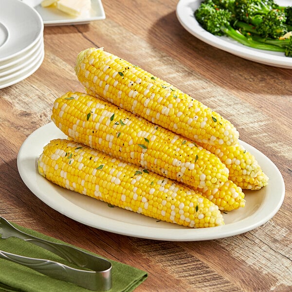 A plate of corn on the cob with butter and broccoli.