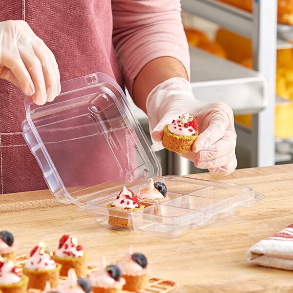 A woman in gloves holding a clear plastic Good Natured container with macarons and treats.