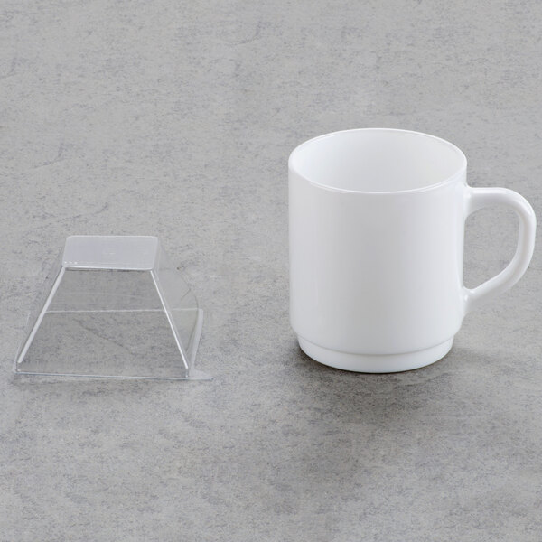 A clear plastic dome lid on a table next to a white mug with a handle.