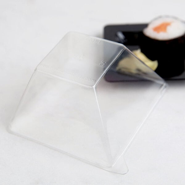 A sushi roll on a clear plastic container with a pyramid-shaped clear plastic lid.