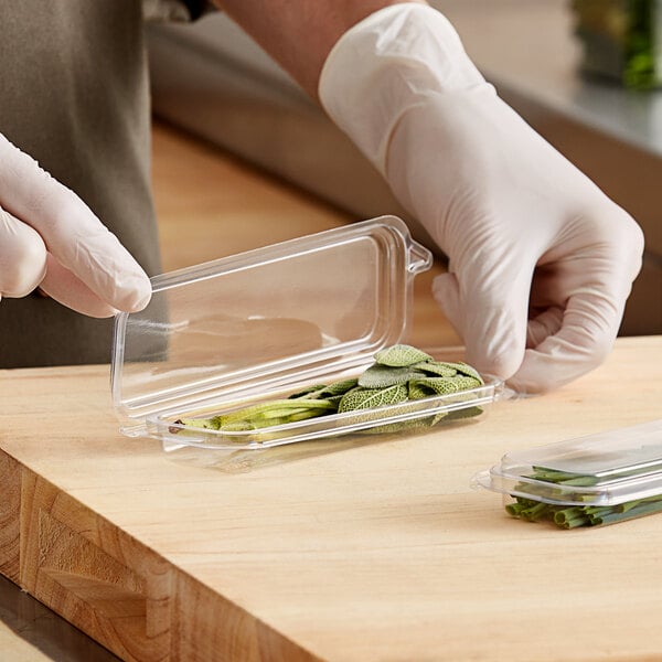 A person holding a Good Natured clear plastic container with green herbs inside.