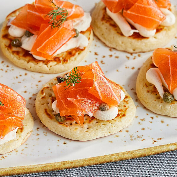 A plate of Beleaf plant-based smoked salmon on crackers with cream cheese and orange slices.