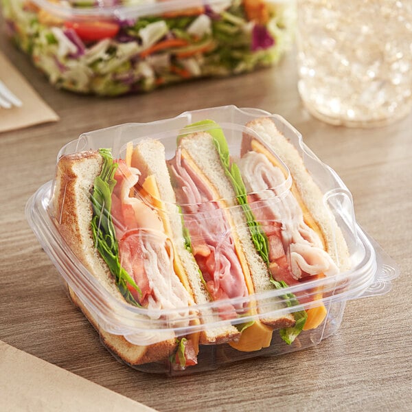 A Good Natured clear plastic container with a sandwich inside, next to a salad.
